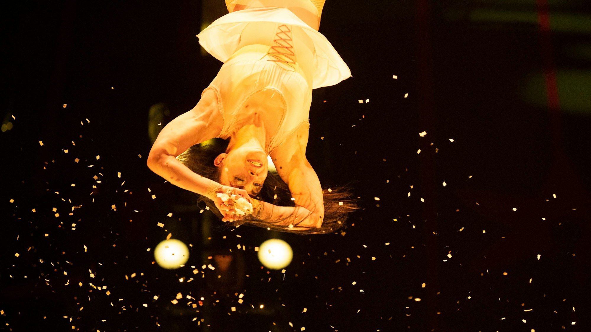 Eine Frau hängt kopfüber im Bild, um sie herum fliegt Konfetti.