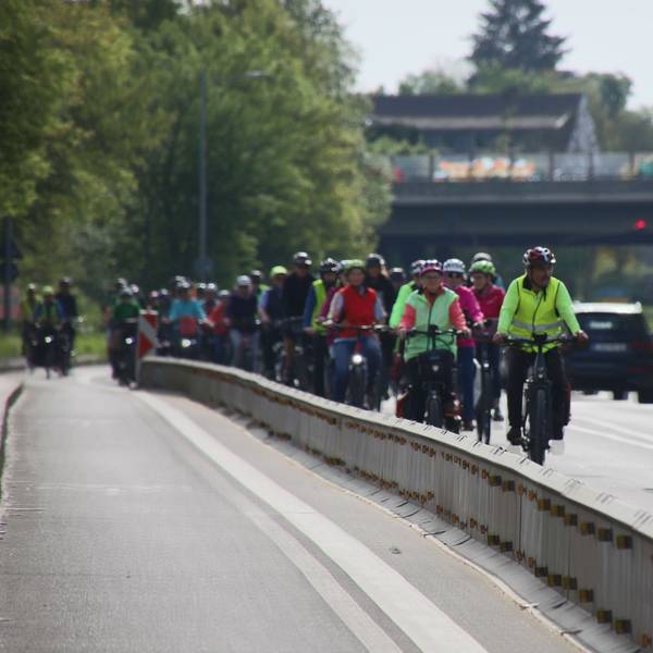 Ein dichter Pulk von Fahrradfahrern, begleitet von Polizei auf einem Motorrad.