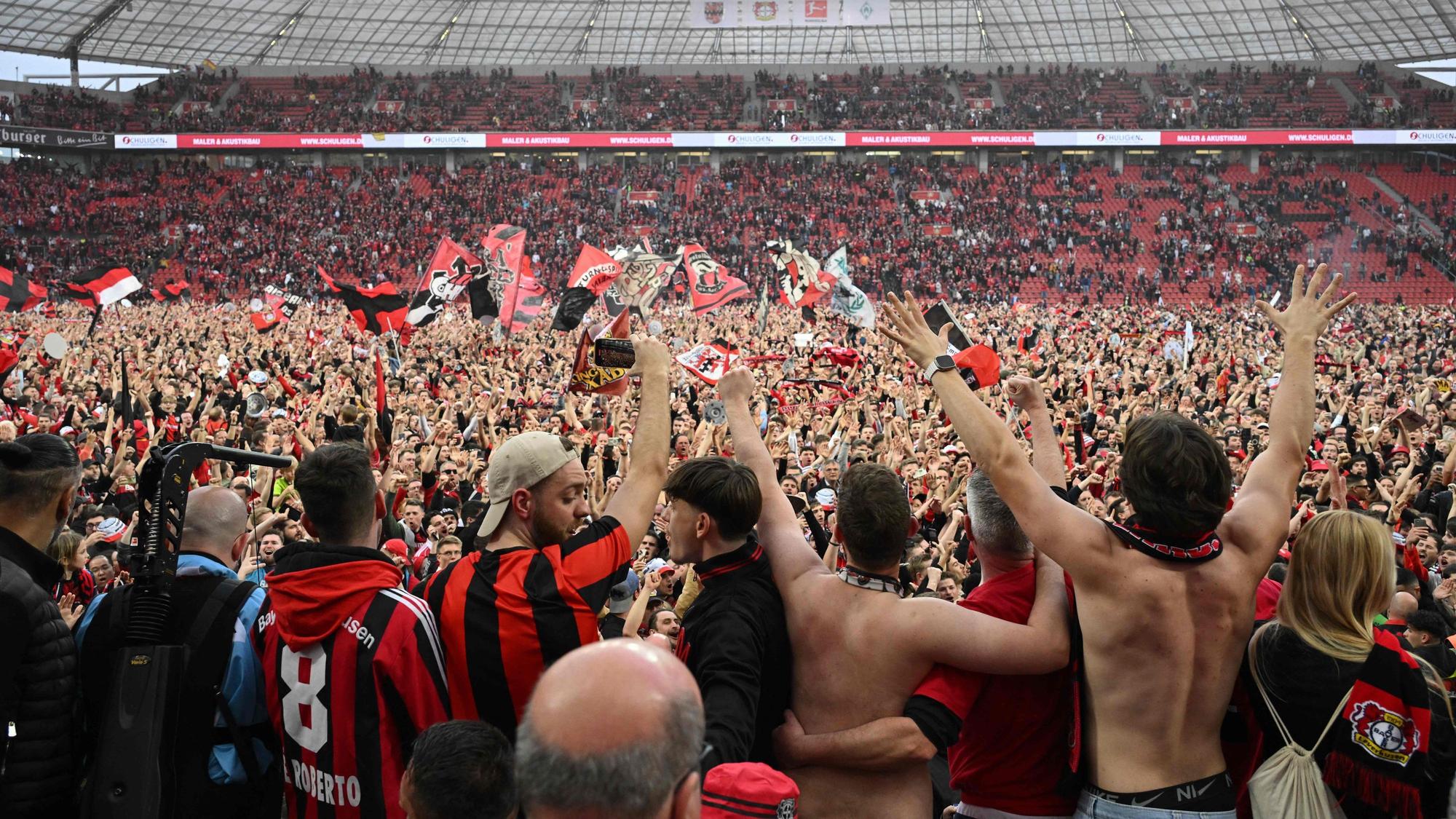 Leverkusen fans celebrate on the pitch after the German first division Bundesliga football match Bayer 04 Leverkusen v Werder Bremen in Leverkusen, western Germany, on April 14, 2024. Bayer Leverkusen were crowned 2023-24 Bundesliga champions for the first time on April 14, 2024. (Photo by INA FASSBENDER / AFP) / DFL REGULATIONS PROHIBIT ANY USE OF PHOTOGRAPHS AS IMAGE SEQUENCES AND/OR QUASI-VIDEO