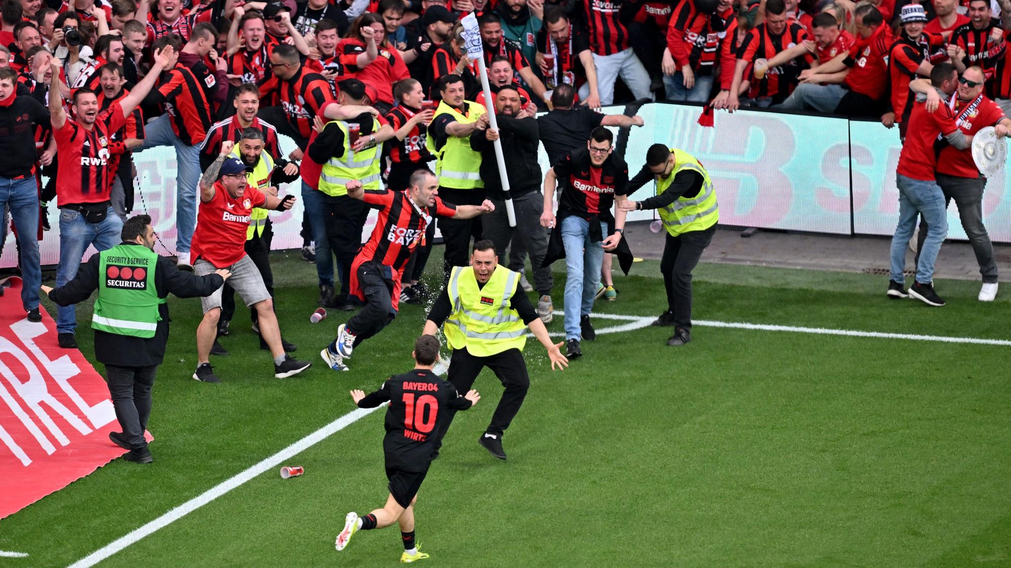 dpatopbilder – 14.04.2024, Nordrhein-Westfalen, Leverkusen: Fußball: Bundesliga, Bayer 04 Leverkusen – SV Werder Bremen, 29. Spieltag, BayArena. Leverkusens Florian Wirtz (vorne M, #10) dreht nach seinem Tor zum 4:0 jubelnd ab und beruhigt Fans und Sicherheitspersonal, die auf das Spielfeld laufen. WICHTIGER HINWEIS: Gemäß den Vorgaben der DFL Deutsche Fußball Liga bzw. des DFB Deutscher Fußball-Bund ist es untersagt, in dem Stadion und/oder vom Spiel angefertigte Fotoaufnahmen in Form von Sequenzbildern und/oder videoähnlichen Fotostrecken zu verwerten bzw. verwerten zu lassen. Foto: David Inderlied/dpa +++ dpa-Bildfunk +++