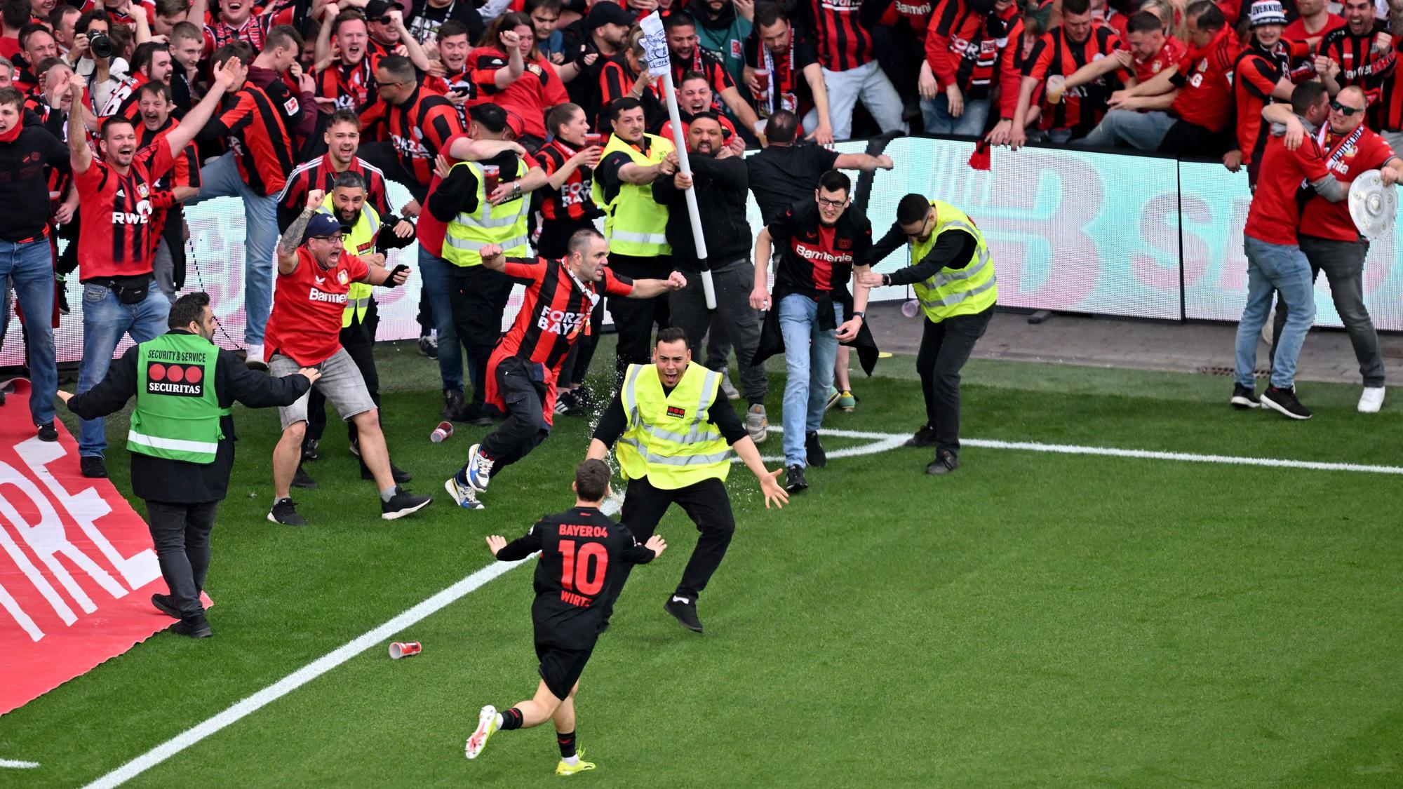 Leverkusens Florian Wirtz dreht nach seinem Tor zum 4:0 jubelnd ab und beruhigt Fans und Sicherheitspersonal, die auf das Spielfeld laufen.