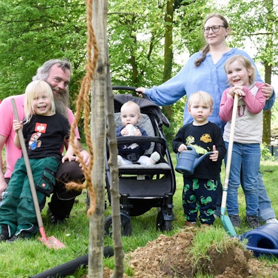 Eine Familie mit vier Kindern pflanzt einen Baum.