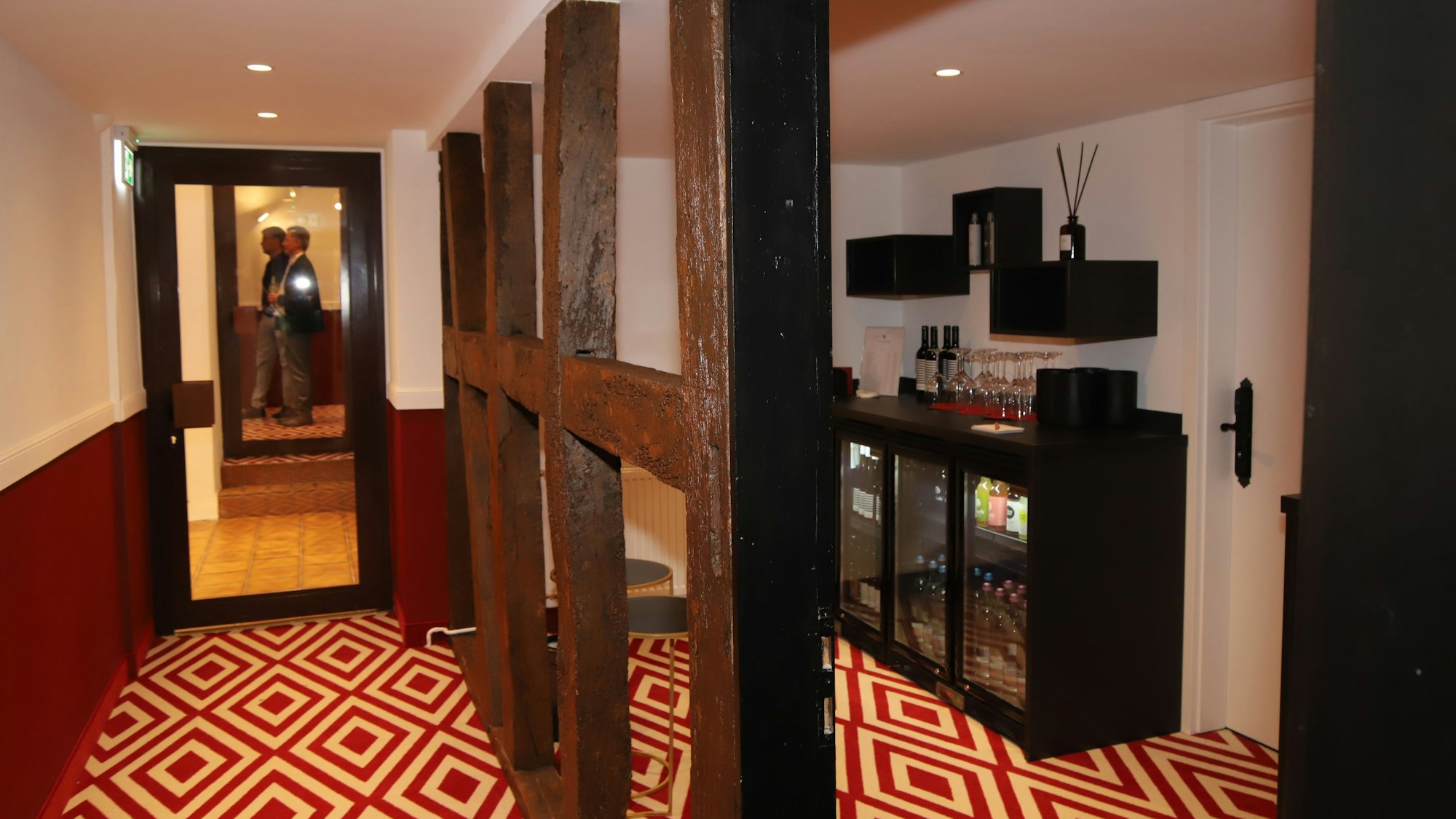 Dunkle Fachwerkbalken stehen vor einer beleuchteten Getränkevitrine.