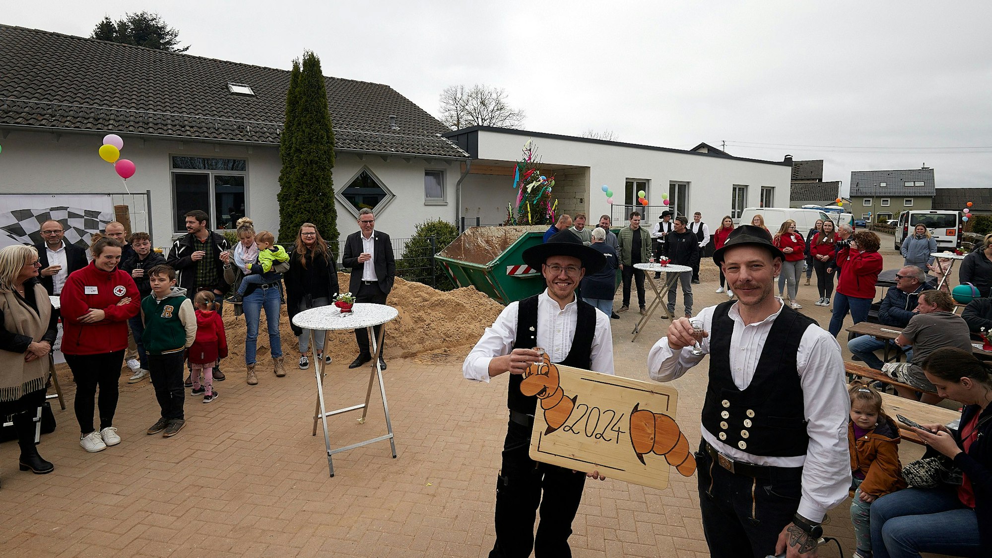 Tobias Kügler steht vorne rechts mit einem Glas in der Hand. Neben ihm steht ein Kollege von ihm, drumherum Zuschauer.