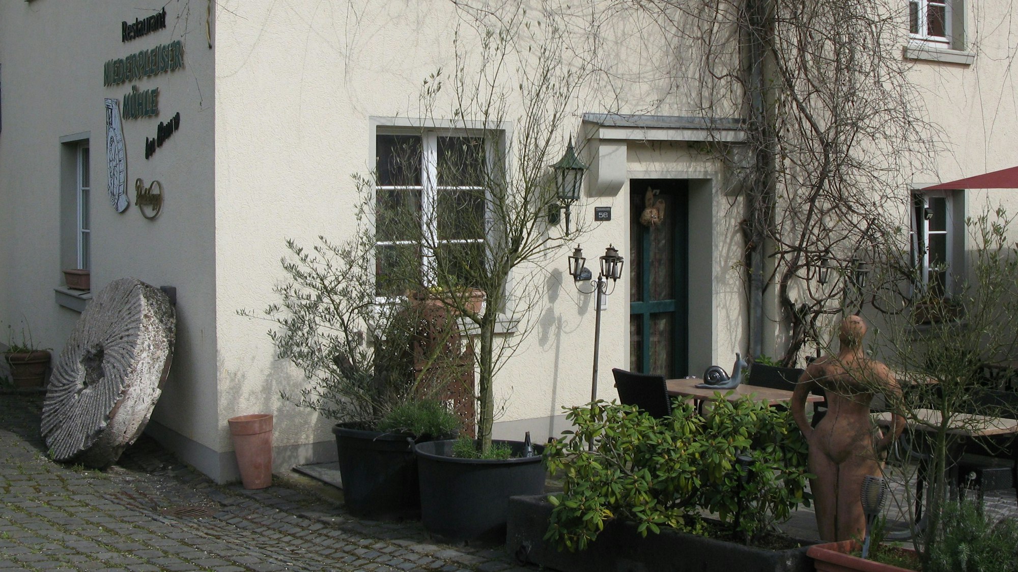 An einer Hauswand lehnt ein altes steinernes Mühlrad.