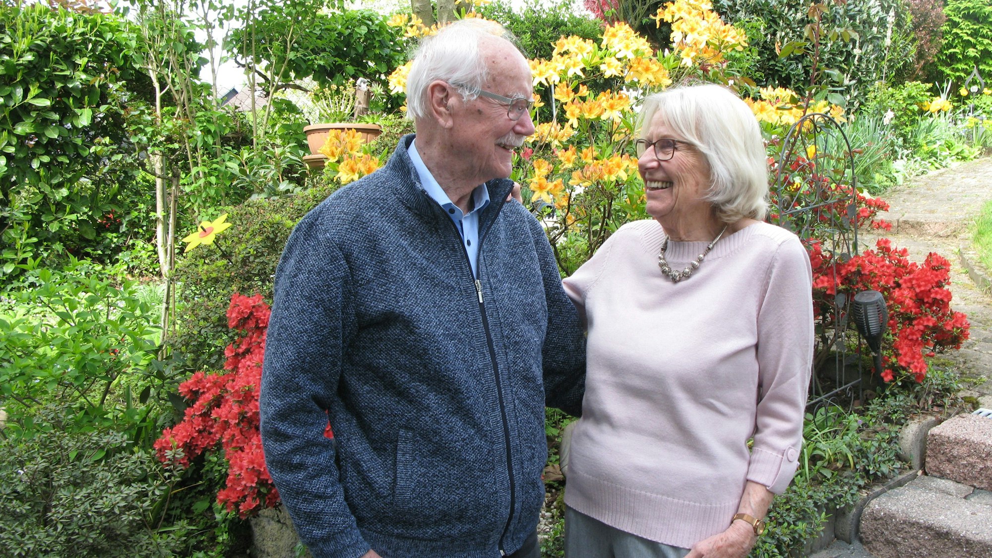 Das Diamanthochzeitspaar Ertzinger steht auf einer Terrasse vor rot und gelb blühenden Pflanzen.