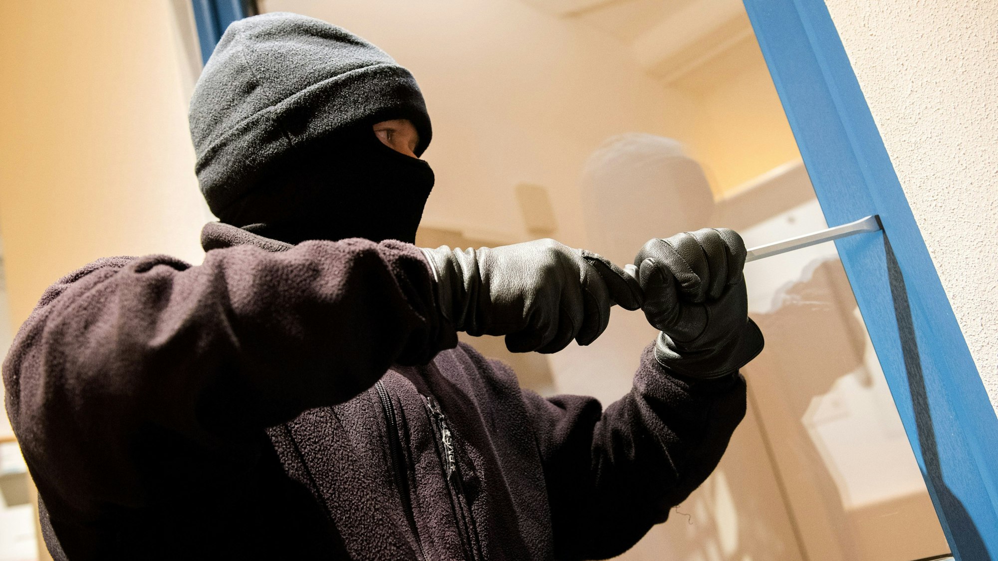 Ein vermummter Einbrecher hebelt ein Fenster auf.
