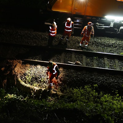 Arbeiter auf Bahngleisen stehen neben einem Baumstamm.