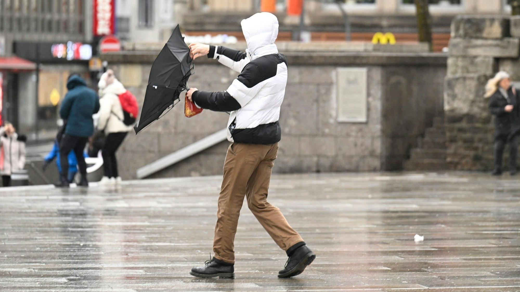 Ein Mann kämpft bei stürmischem Wetter am Kölner Dom mit seinem Regenschirm. Teils schwere Sturmböen von 80 bis 100 km/h sind im Zuge der aufkommenden Unwetter am Wochenende möglich.