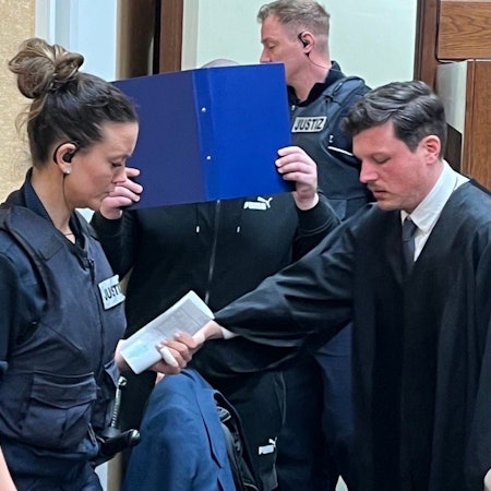 Der Angeklagte mit Wachtmeistern und Verteidiger Philipp Stangier beim Prozessauftakt im Landgericht Köln