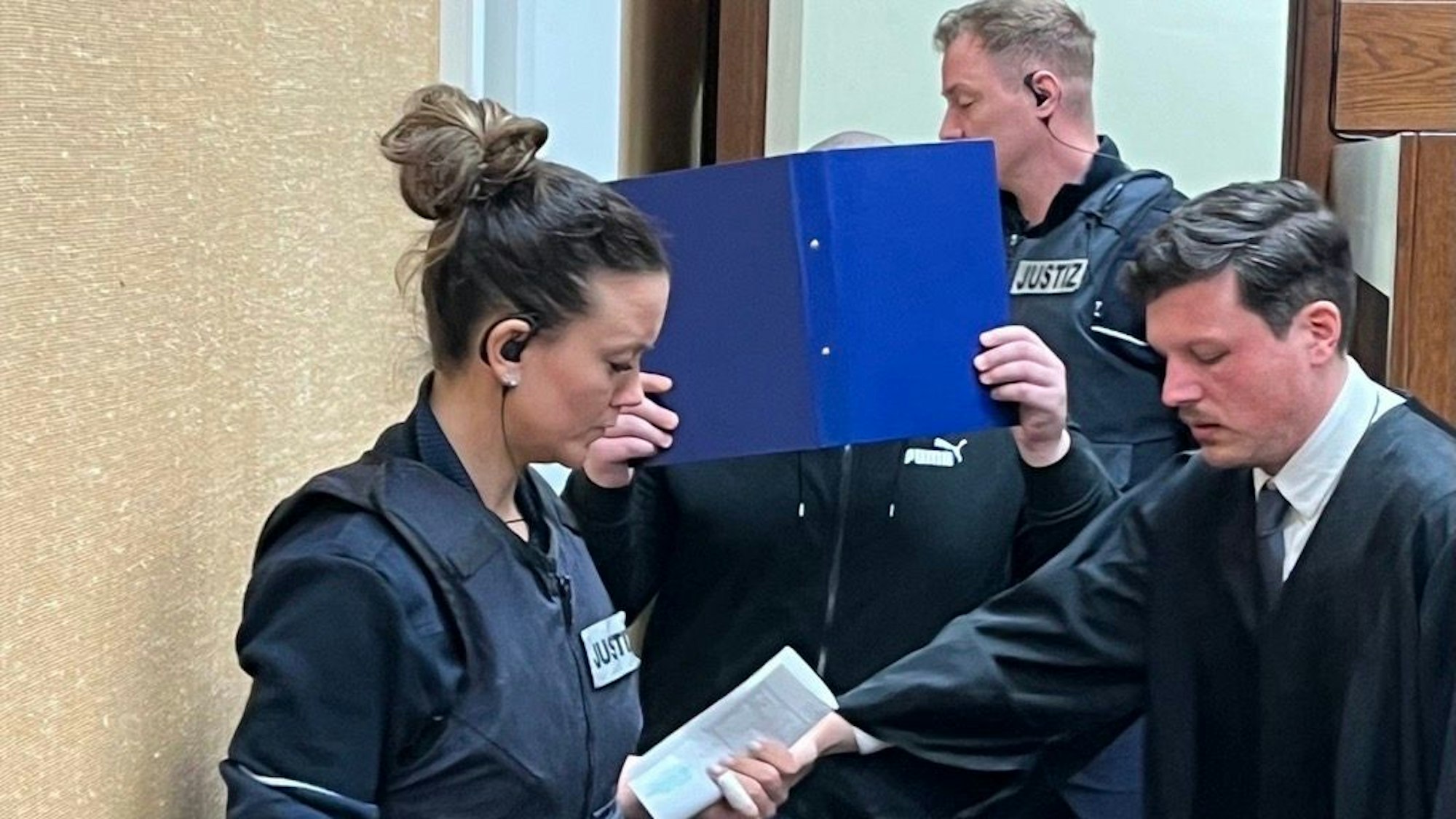 Der Angeklagte mit Wachtmeistern und Verteidiger Philipp Stangier beim Prozessauftakt im Landgericht Köln
