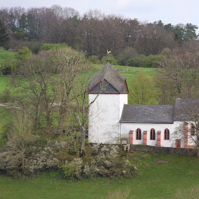 Die Alte Kirche von außen betrachtet: umgeben von Wiesen und einigen Bäumen.