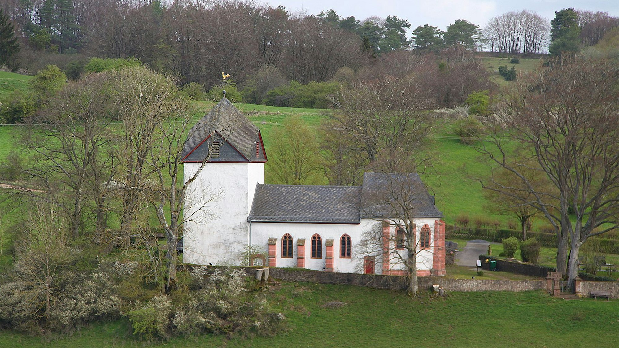 Die Alte Kirche von außen betrachtet: umgeben von Wiesen und einigen Bäumen.