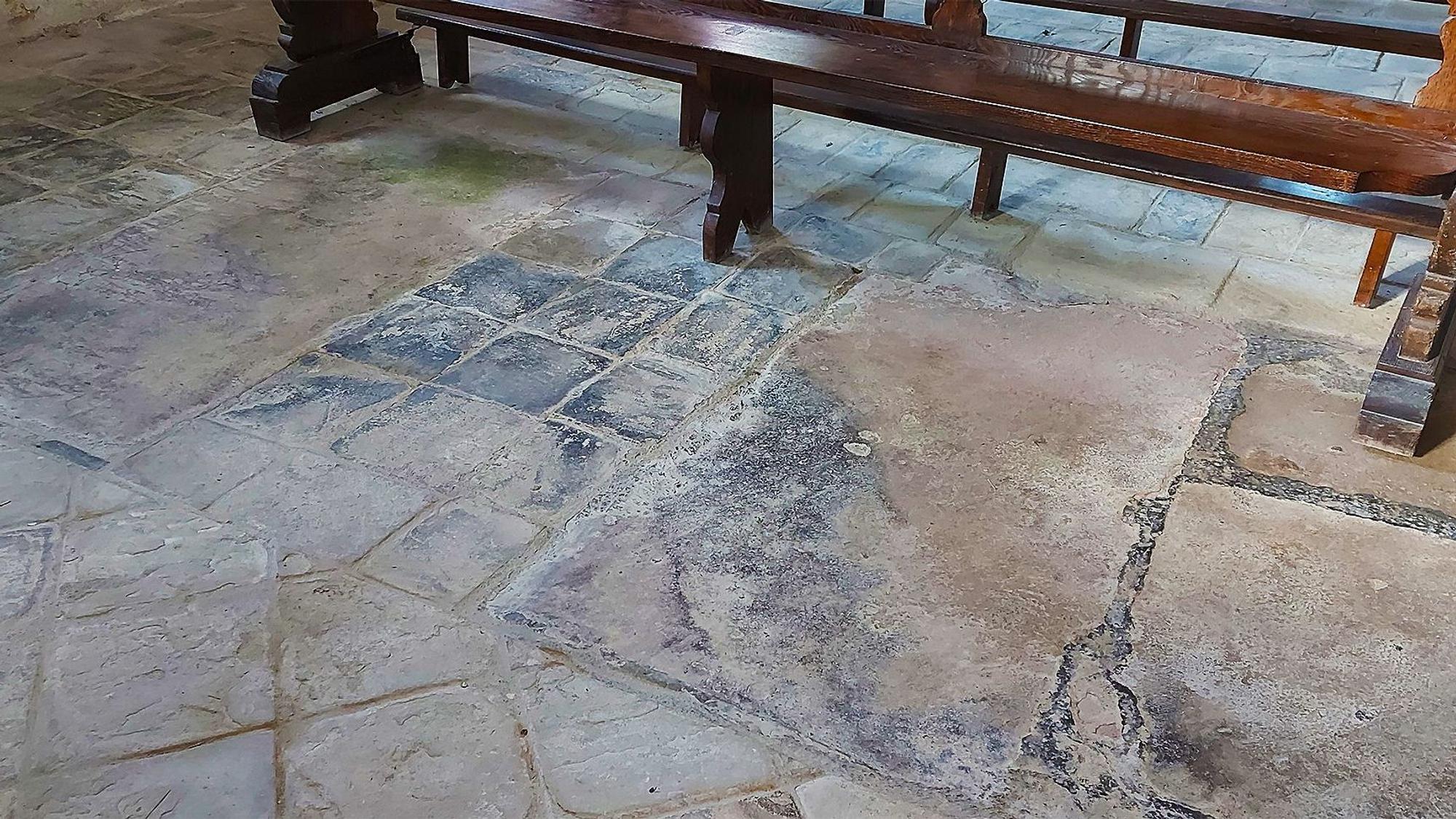 Zwei Grabplatten sind zu sehen, getrennt durch wesentlich kleinere quadratische Sandsteinplatten. Im Hintergrund steht eine Kirchenbank.