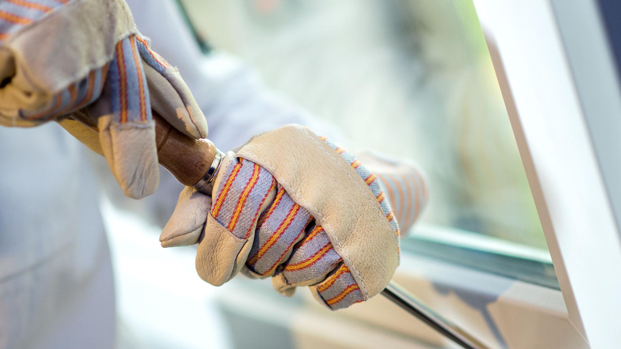 Zwei Hände in Handschuhen hebeln ein Fenster auf.