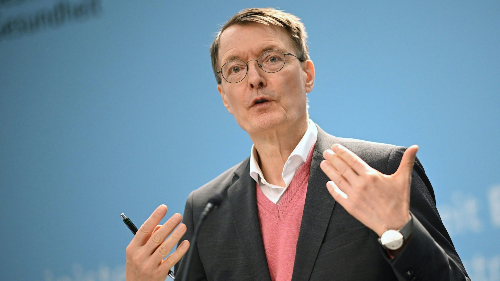 Bundesgesundheitsminister Karl Lauterbach (SPD) während einer Pressekonferenz auf einer Bühne. Er trägt ein Sakko und einen lachsfarbenen Pollunder.