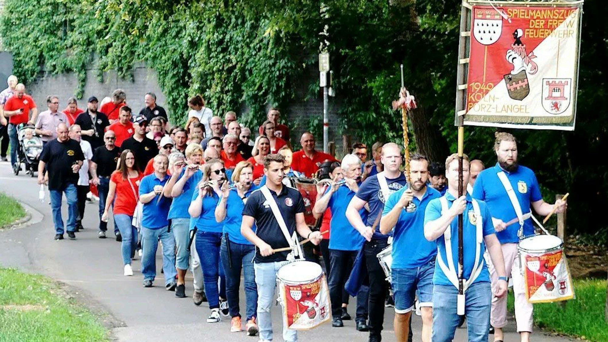 Menschen, die im Spielmannszug der Freiwilligen Feuerwehr Köln-Porz-Langel aktiv sind, ziehen mit ihren Instrumenten durch Porz.