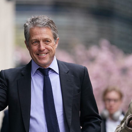 Hugh Grant lächelt und winkt.