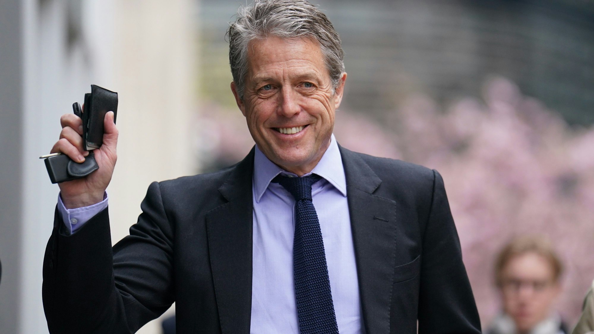 Hugh Grant lächelt und winkt.