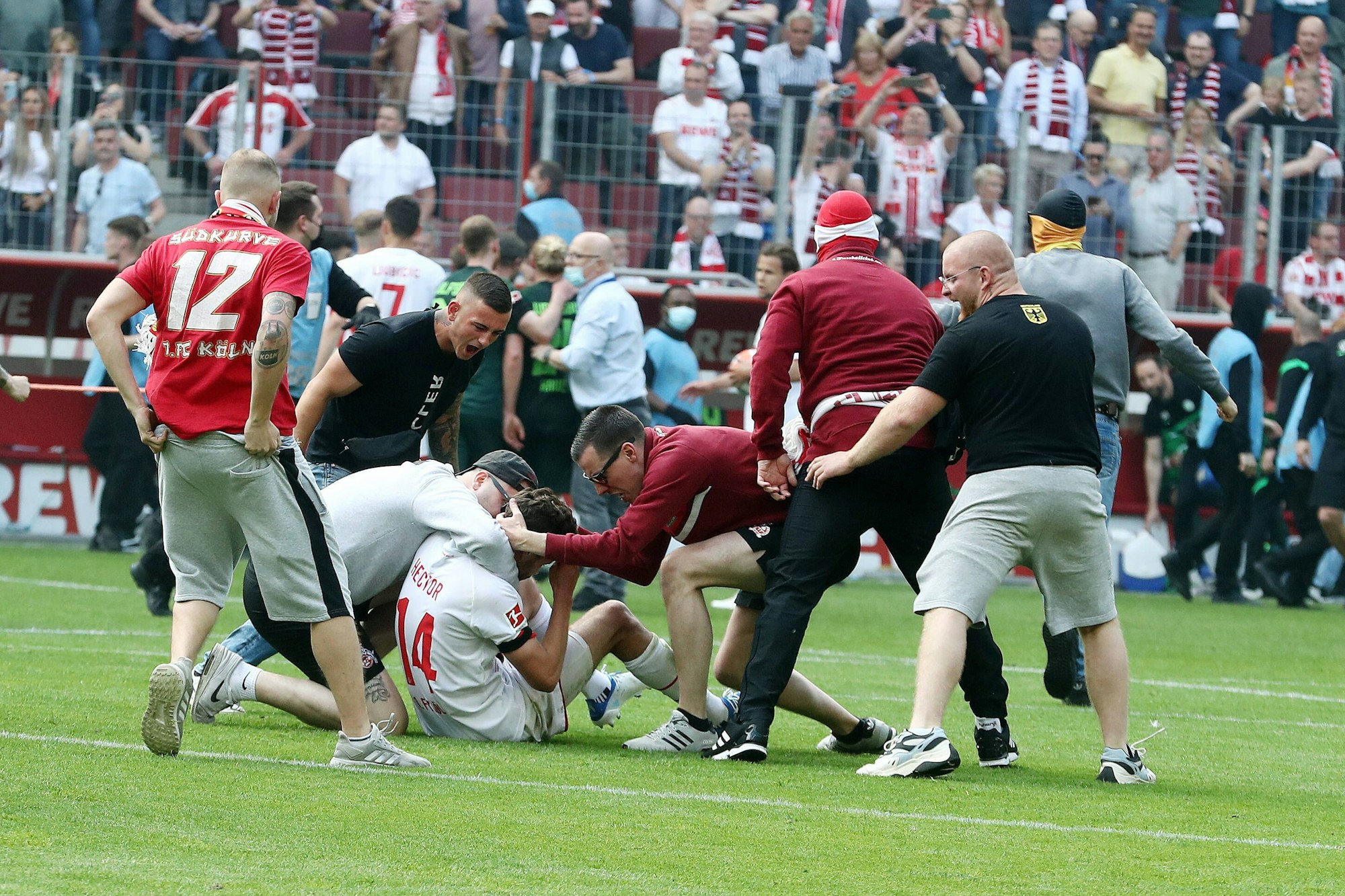 Jonas Hector sitzt nach der Heimniederlage gegen Wolfsburg im Mai 2022 sichtlich angefressen auf dem Boden - die jubelnden Fans scheint das nicht zu stören. Zwei Fans beugen sich zu Hector runter und versuchen ihn zu umarmen.