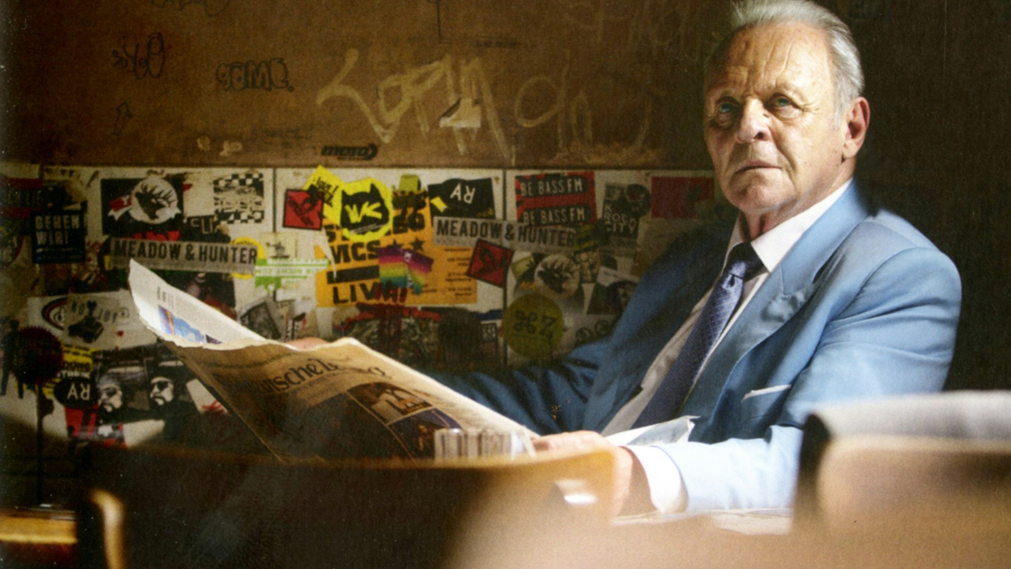 Anthony Hopkins sitzt mit einer Zeitung an einem Tisch im Stiefel.