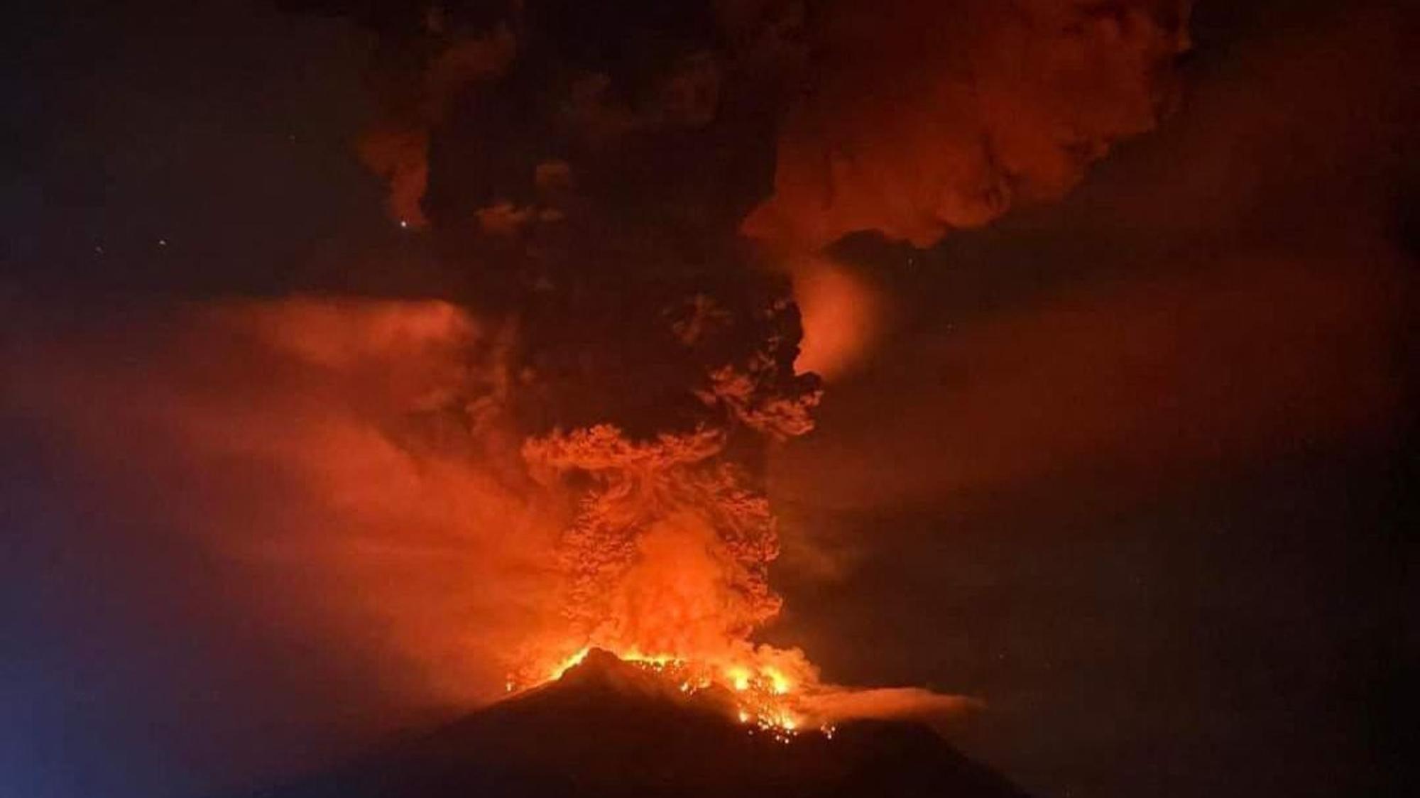 Ein Vulkan stößt bei Dunkelheit dichten Rauch aus, der von austretender Lava auf der Spitze rot erleuchtet wird.