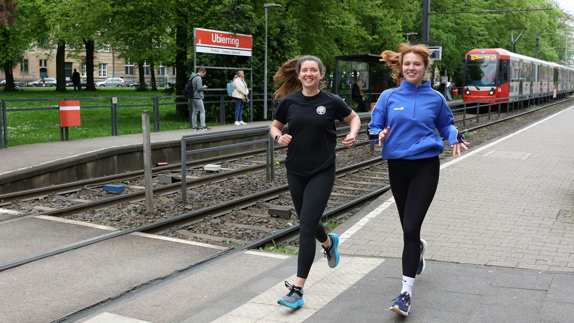 Die Kölnerinnen Katharina Oeltermann und Sophia Staudinger tragen Sportkleidung und laufen an der KVB-Haltestelle Ubierring entlang.
Foto von Martina Goyert