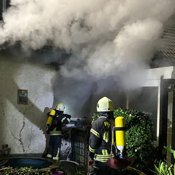 Unter schwerem Atemschutz gehen Feuerwehrleute gegen das Feuer in einem brennenden Haus in Overath-Untereschbach vor.