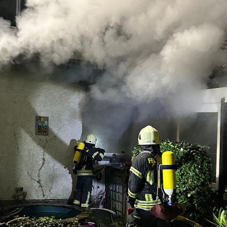 Unter schwerem Atemschutz gehen Feuerwehrleute gegen das Feuer in einem brennenden Haus in Overath-Untereschbach vor.