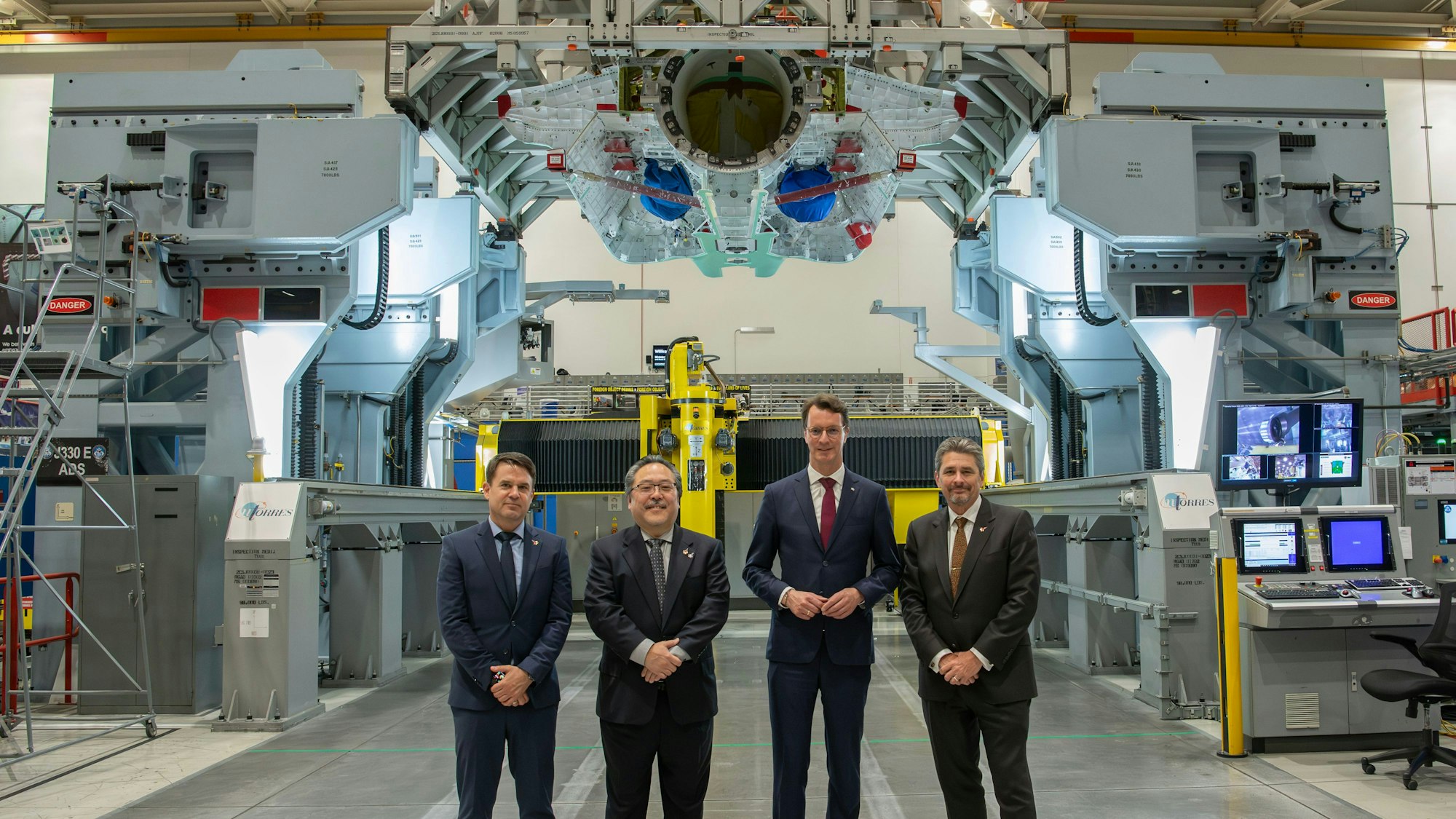 Hendrik Wüst und Industrievertreter sind in einem Werk im Gruppenbild zu sehen.