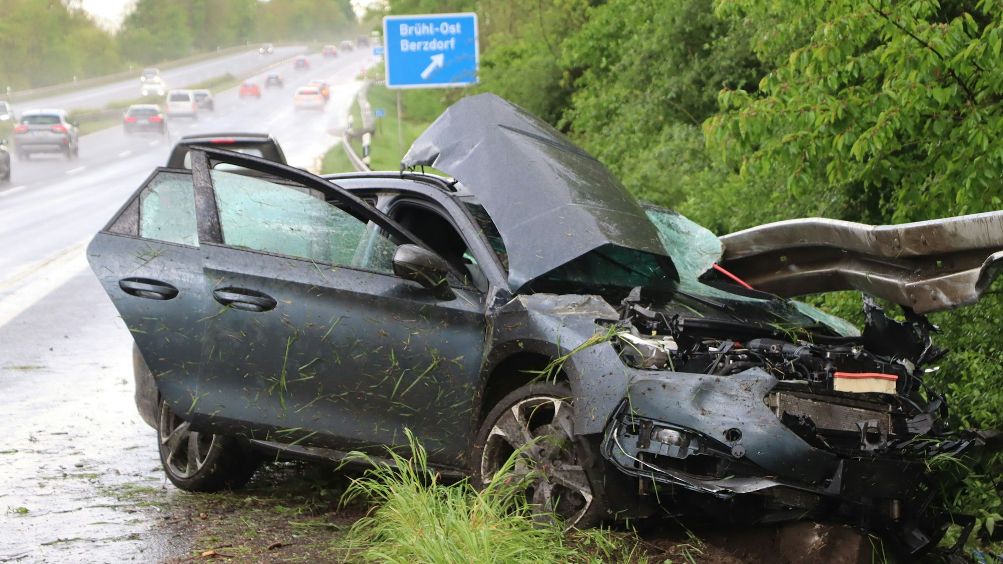Ein dunkes Auto liegt zerbeult am Seitenstreifen in der Leitplanke.