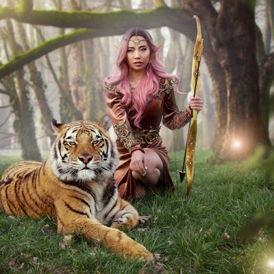 Eine Frau trägt Elfenohren und posiert mit einem ausgewachsenem Tiger.