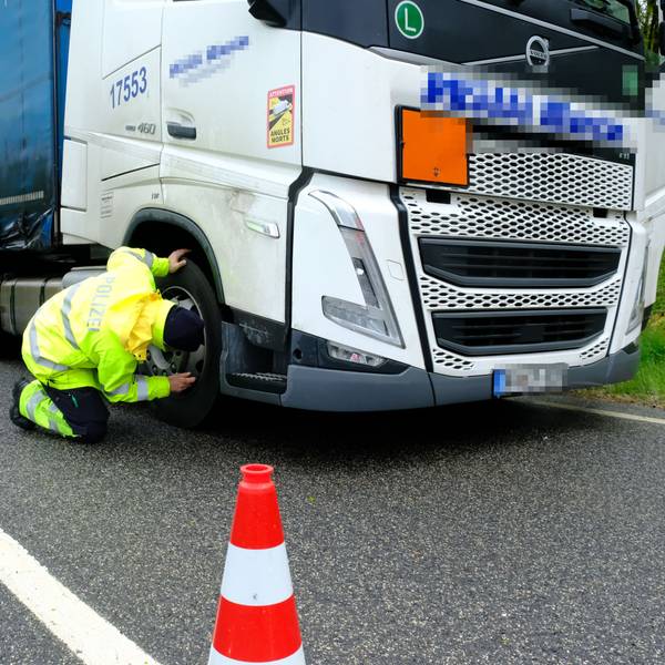 Ein Polizeibeamter in signalgelber Kleidung überprüft die Bremsanlage eines Lastwagens.