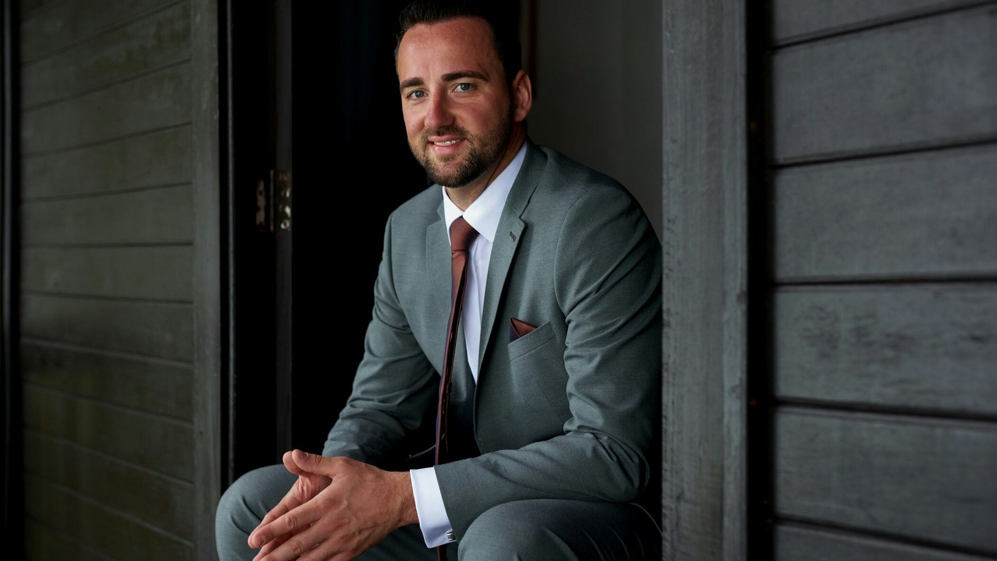 Ein Mann im Anzug vor einer dunkelgrauen Holzfassade.