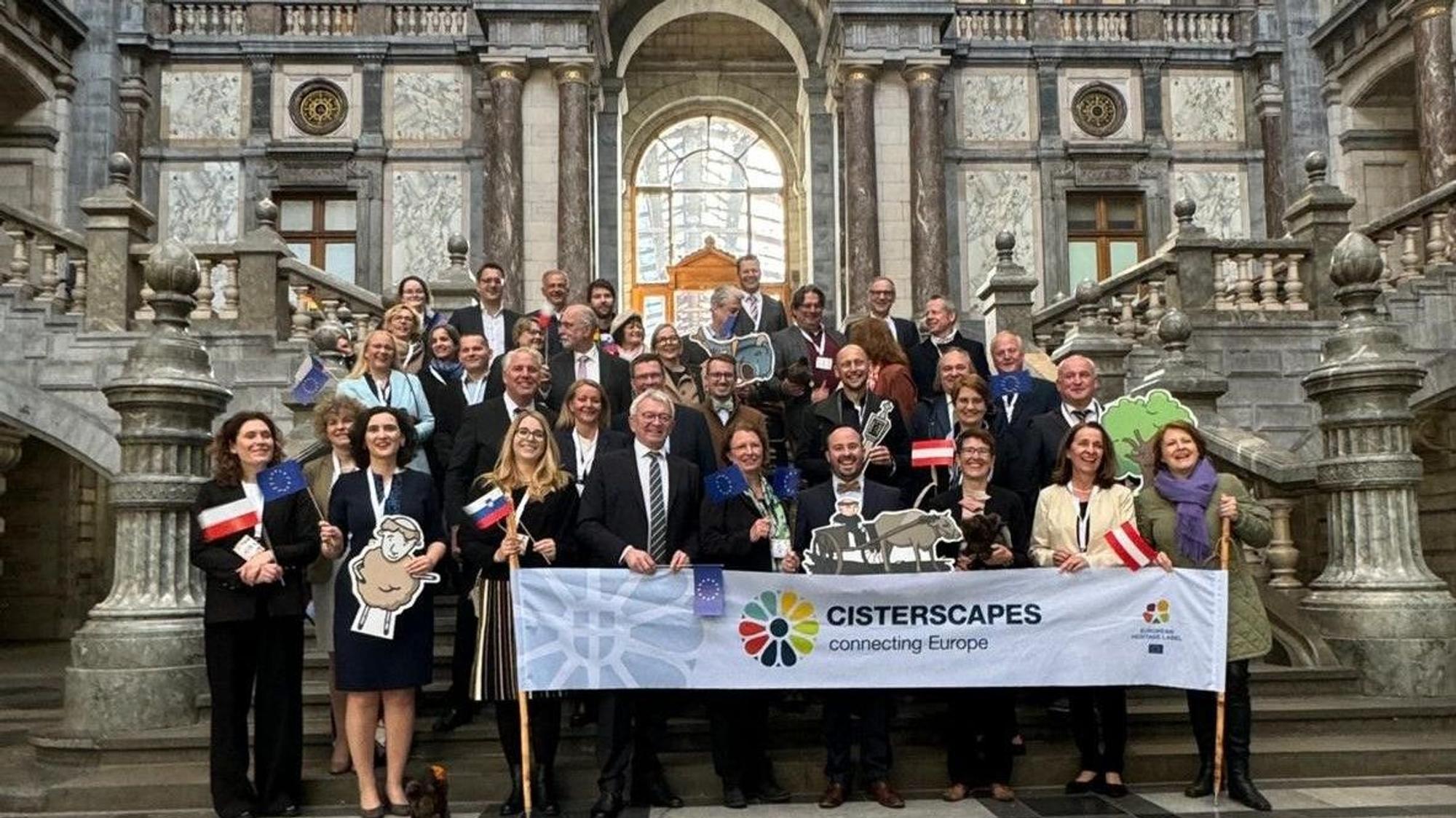 Zahlreiche Menschen stehen auf den Stufen eines palastartigen Gebäudes. Davor ein Banner mit der Aufschrift Cisterscapes.