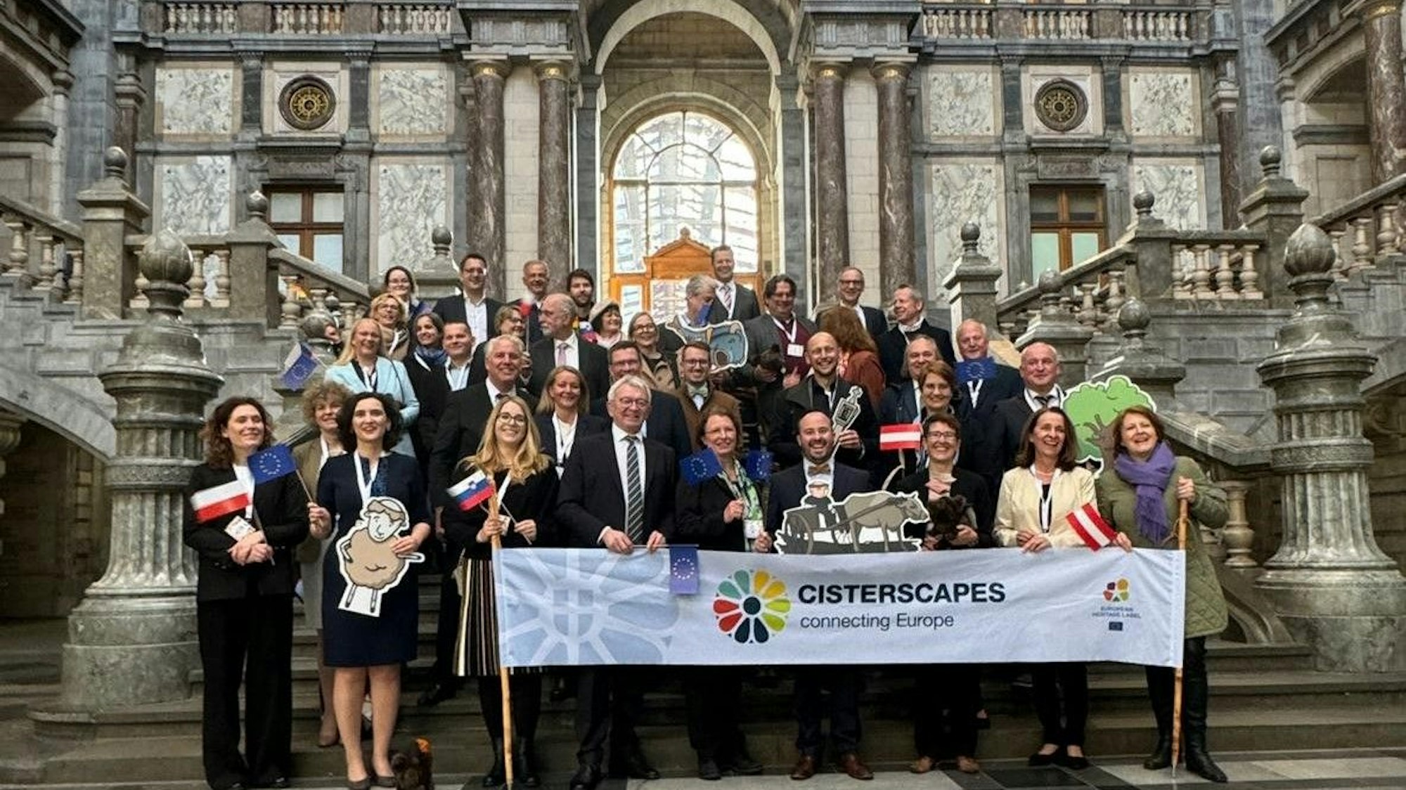 Zahlreiche Menschen stehen auf den Stufen eines palastartigen Gebäudes. Davor ein Banner mit der Aufschrift Cisterscapes.