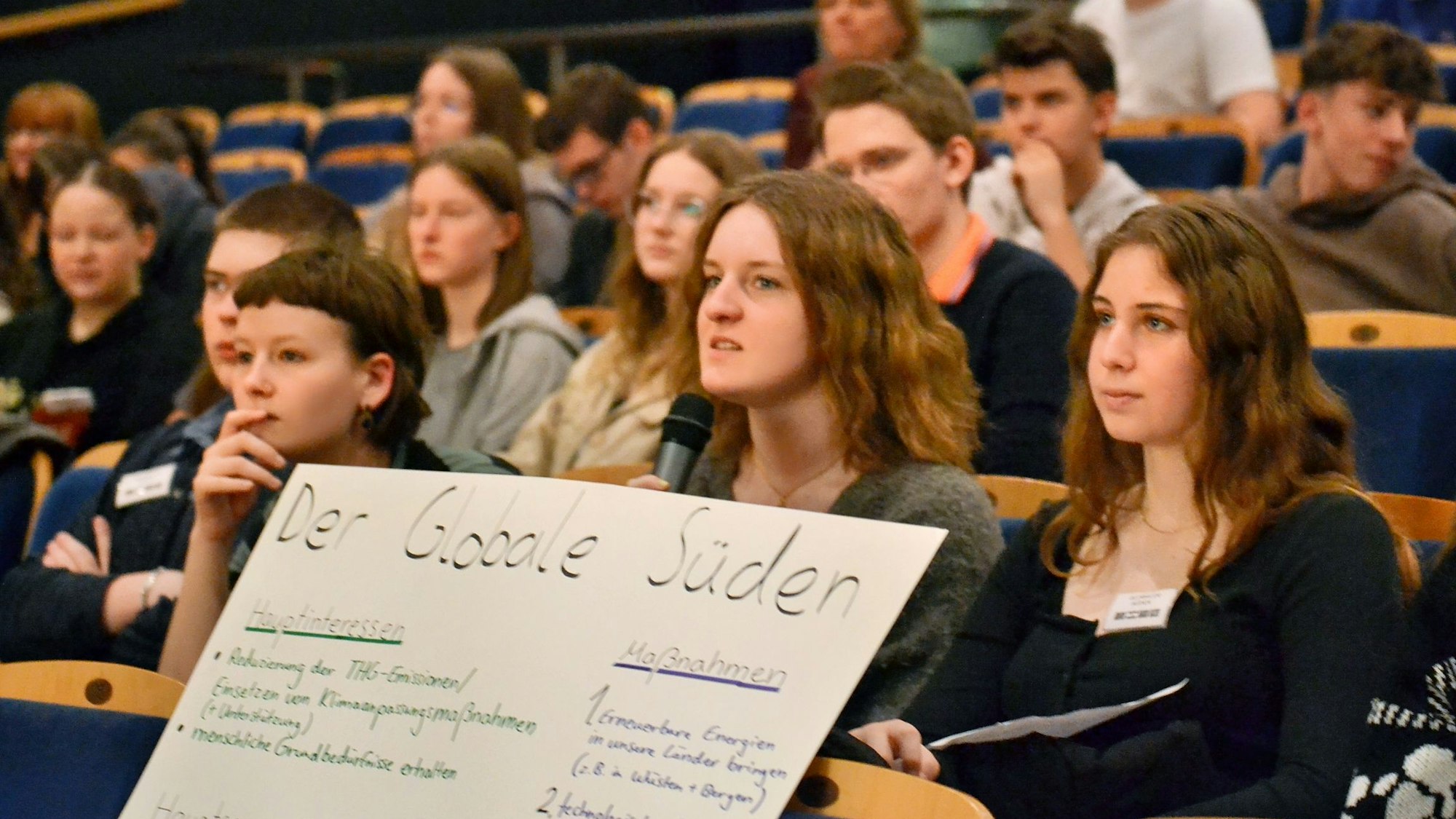 Elftklässler sitzen in der Schulaula, einige halten ein Plakat mit dem Schriftzug „Der Globale Süden“.