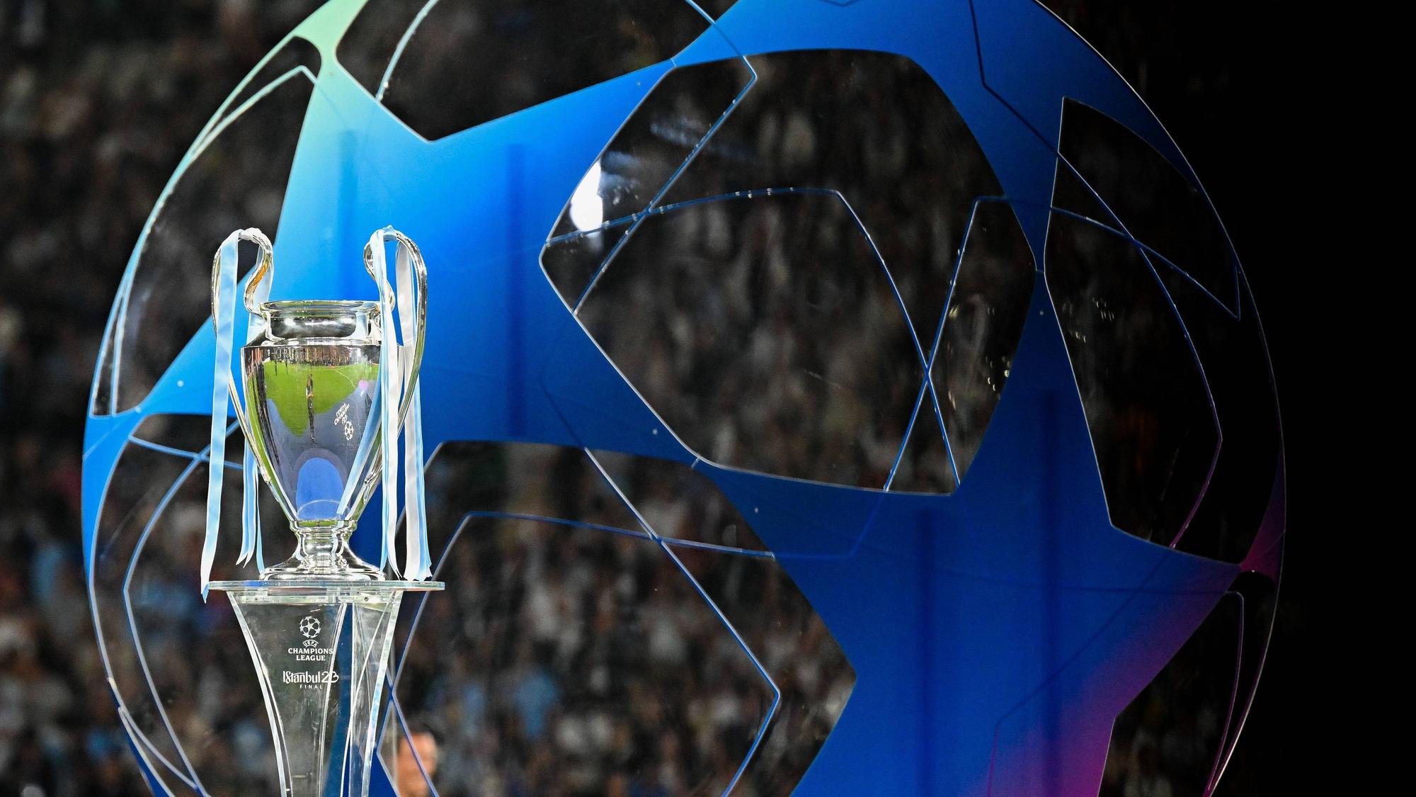 Die Champions League Trophäe steht auf einem Podest. Im Hintergrund ist ein großes blaues Gebilde in Form des Champions League-Balles zu erkennen.