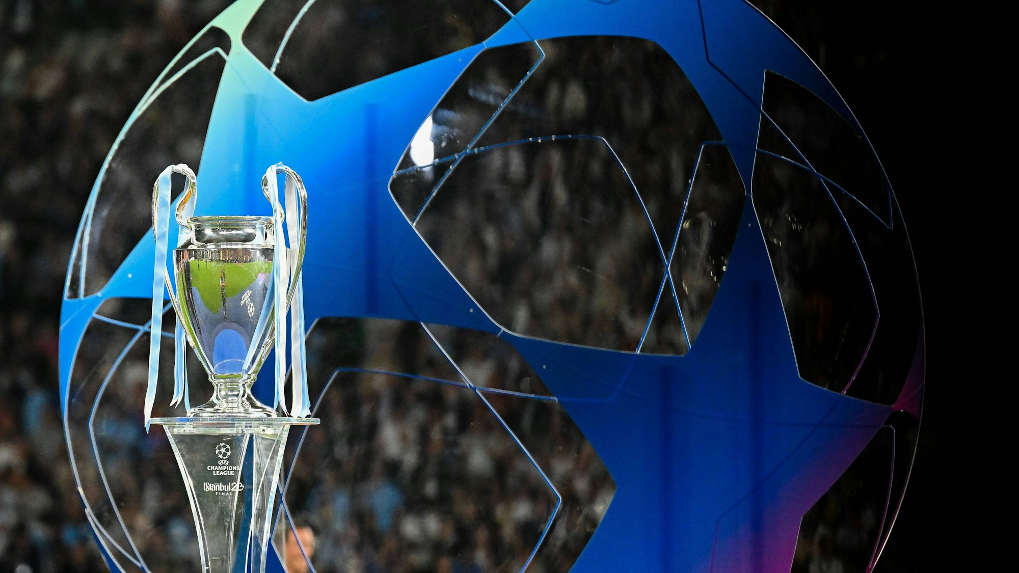 Die Champions League Trophäe steht auf einem Podest. Im Hintergrund ist ein großes blaues Gebilde in Form des Champions League-Balles zu erkennen.