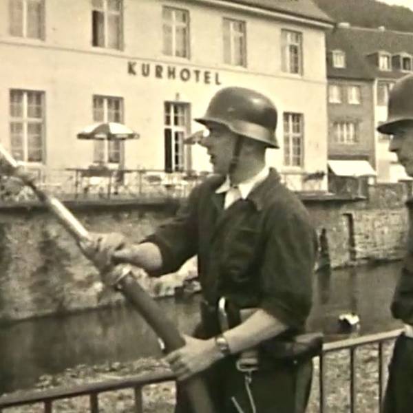 Zwei Feuerwehrleute stehen vor dem ehemaligen Kurhotel, einer hält einen Schlauch.