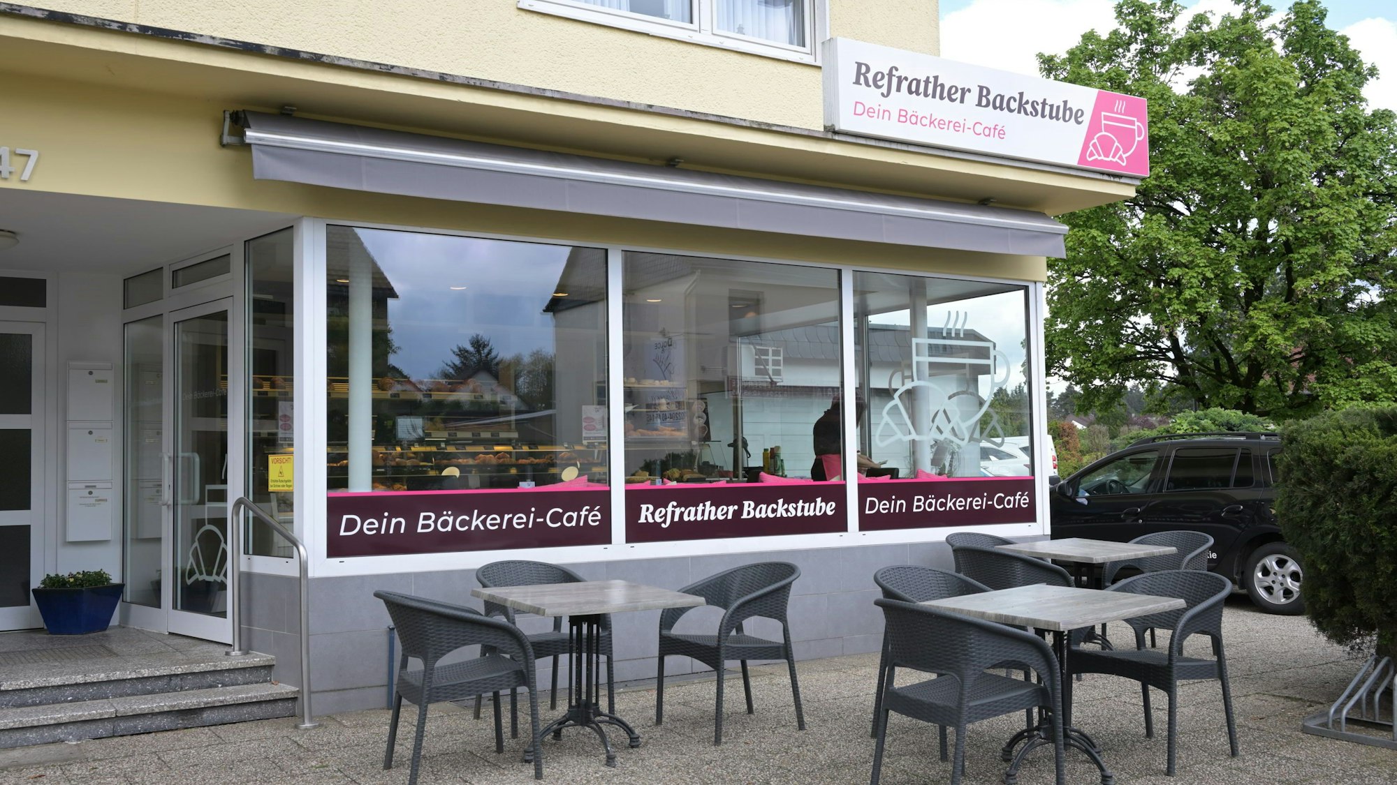 Zu sehen ist die Außenansicht der Bäckerei mit drei Tischen sowie Stühlen vor dem Geschäft.