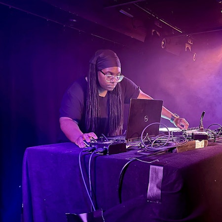 Jlin auf der Bühne des Jaki im Kölner Stadtgarten. Sie trägt eine schwarze Bandana und ein schwarzes T-Shirt, beugt sich über ihren Laptop.