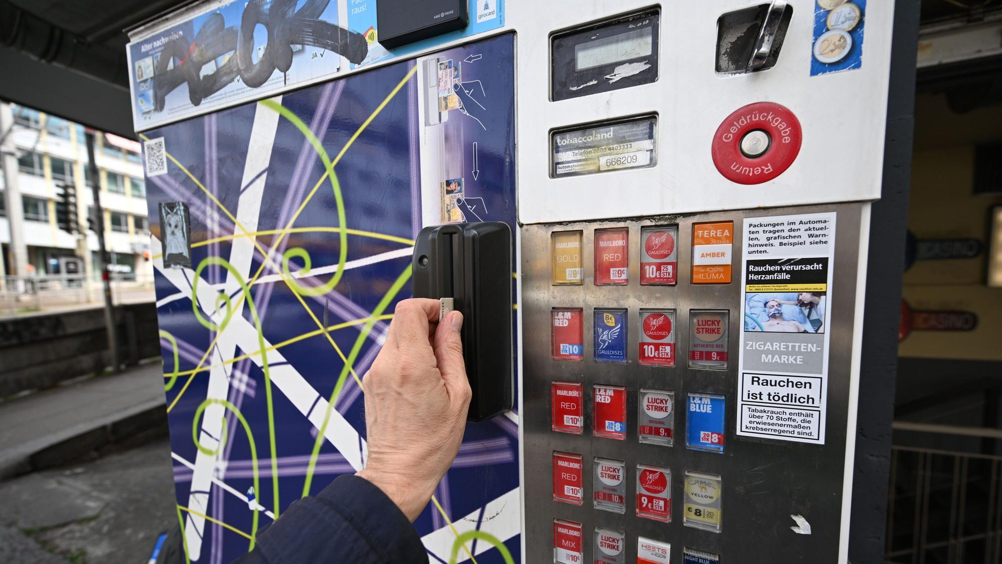 Ein Mann zieht seinen Ausweis durch den Schlitz eines Zigarettenautomaten. Ein solcher ist in Köln-Vingst gesprengt worden. (Symbolbild)