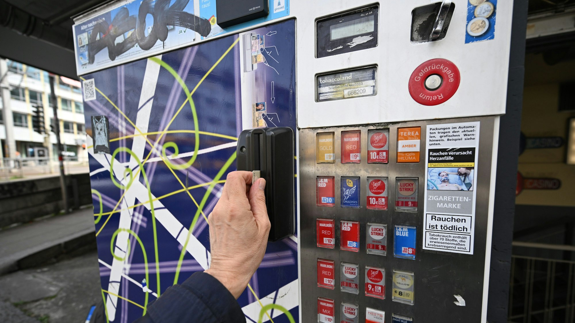 Ein Mann zieht seinen Ausweis durch den Schlitz eines Zigarettenautomaten. Ein solcher ist in Köln-Vingst gesprengt worden. (Symbolbild)