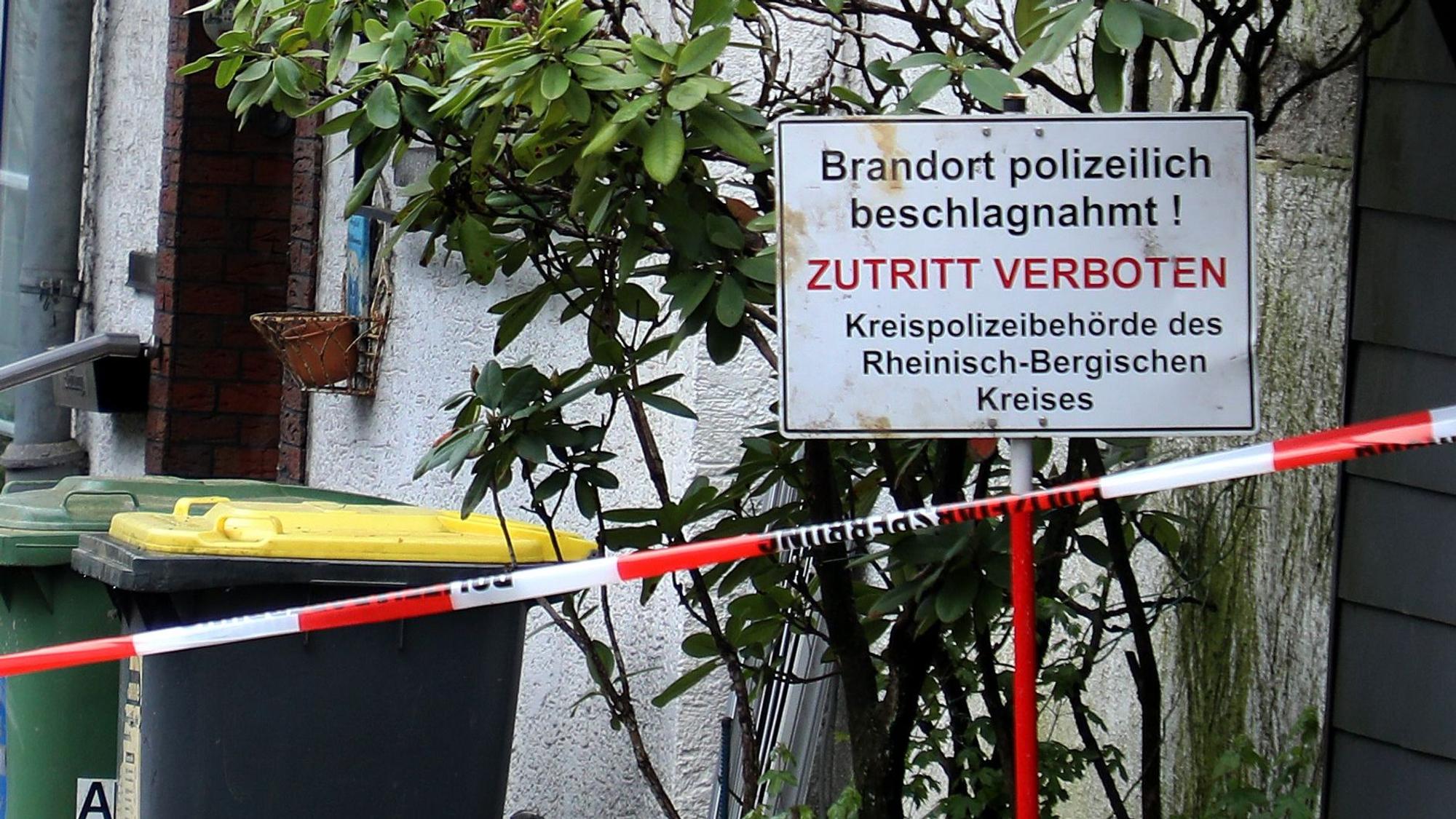 Vor einem Haus steht ein Schild mit der Aufschrift „Brandort polizeilich beschlagnahmt! Zutritt verboten“. Davor ist Polizei-Absperrband zu sehen.