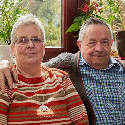 Helene und Klaus Berends sitzen vor einem Fenster, er hat seinen Arm um sie gelegt.