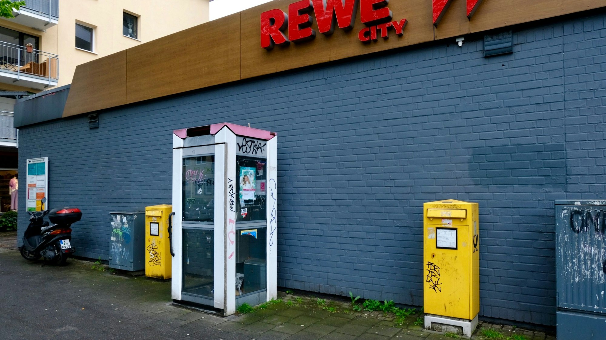 Das Bild zeigt eine verwahrloste und nicht mehr funktionstüchtige Telefonzelle vor dem Rewe-Markt an der Dürener Straße. Foto von Susanne Esch