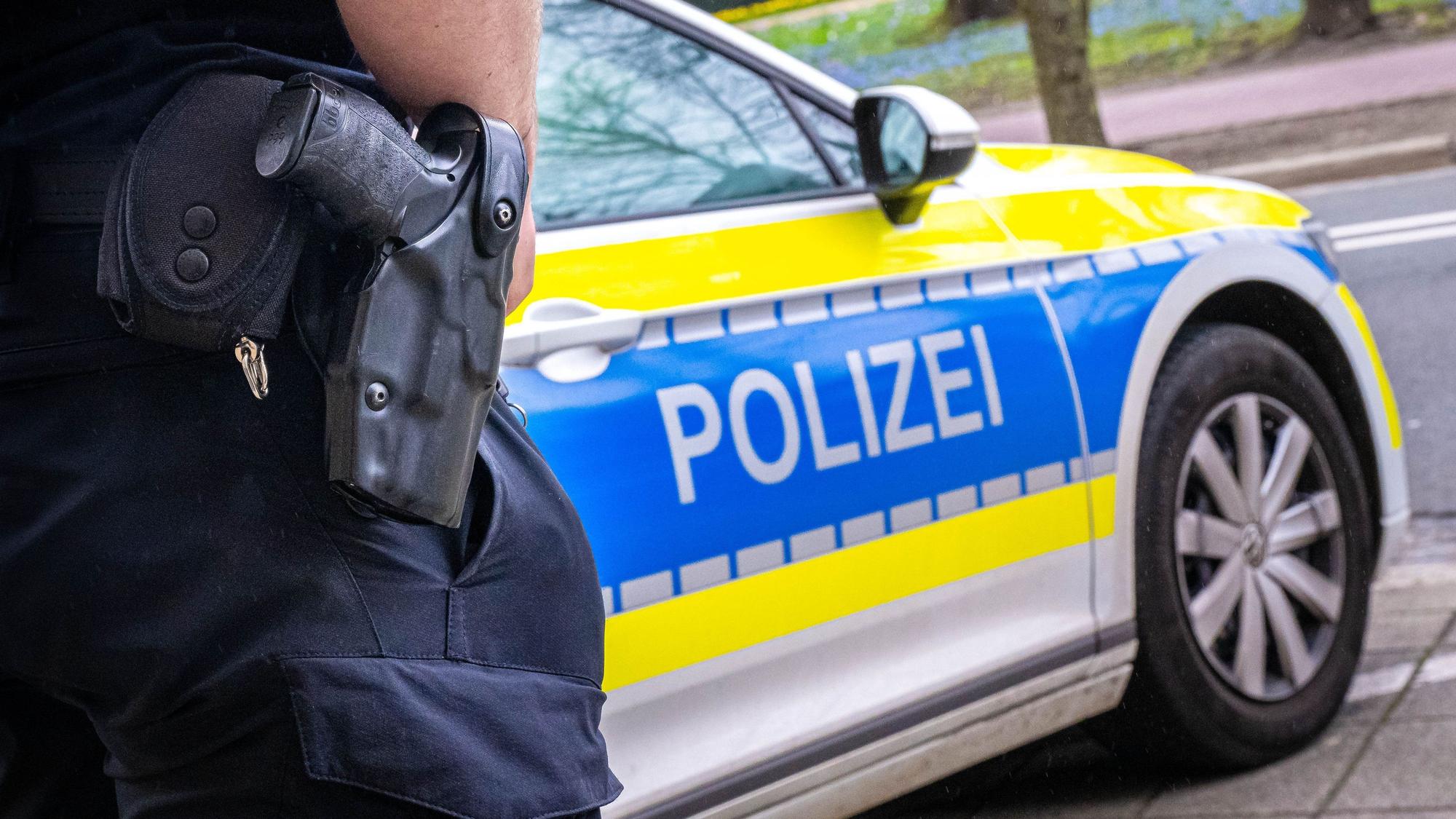 Auf dem Foto ist ein Polizist zu sehen, der vor einem Streifenwagen steht.