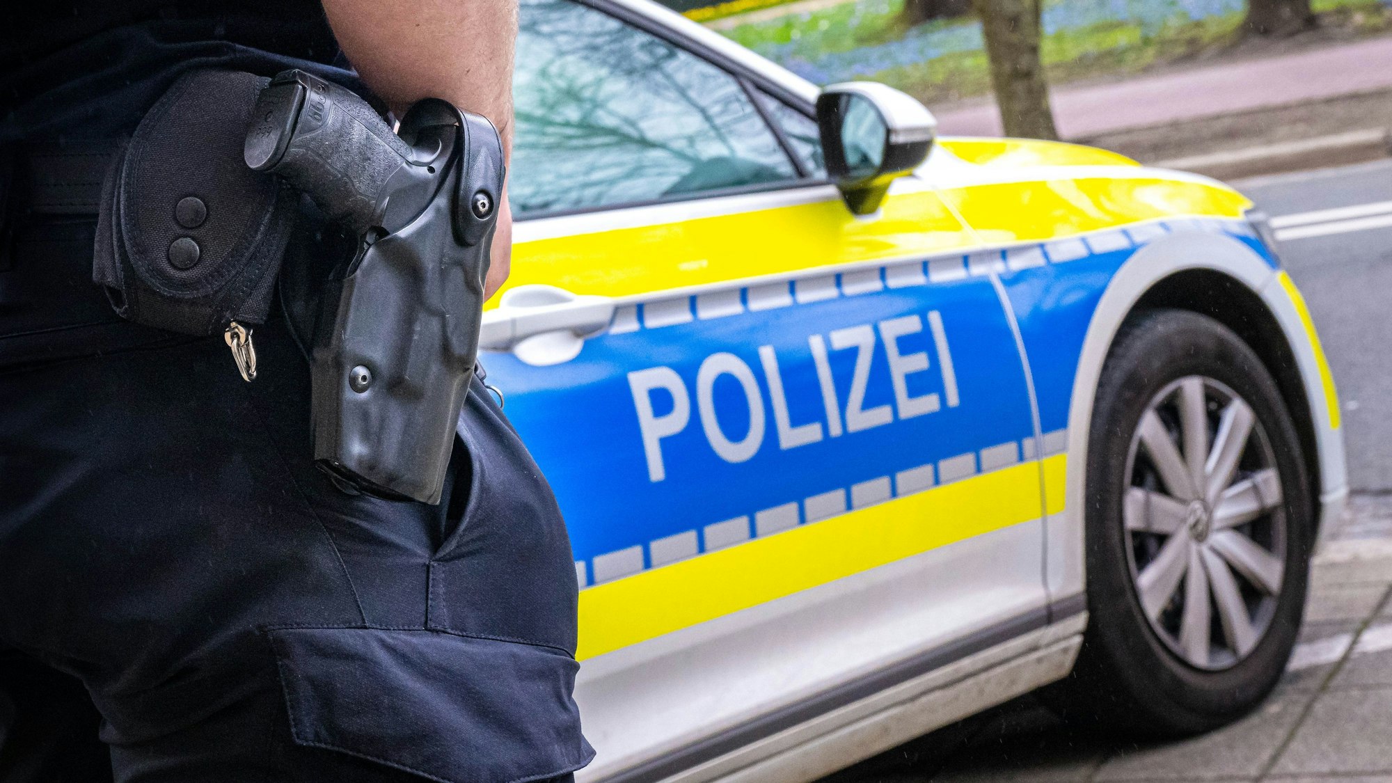 Auf dem Foto ist ein Polizist zu sehen, der vor einem Streifenwagen steht.