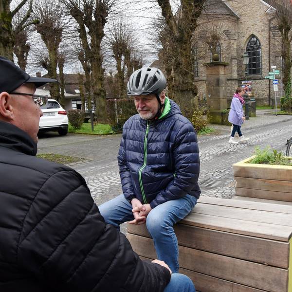 Zwei Männer sitzen auf neuen Bänken an einer Straße in Lindlar.